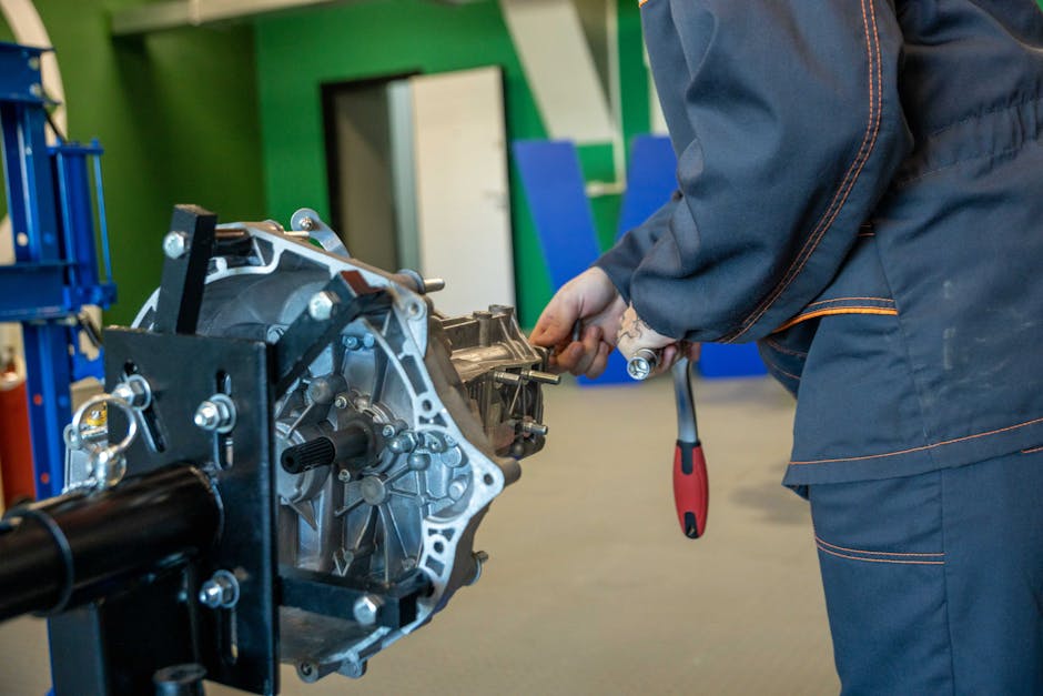 Mechanic uses tools to repair car transmission in an indoor workshop setting.